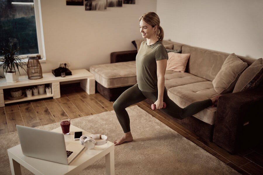 A person doing a dumbbell lunge while following a laptop